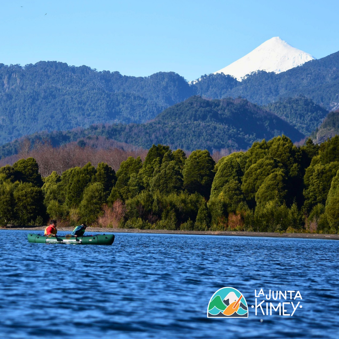 Personas navegando en kayak sobre un lago con vista a un volcán nevado y bosques de Panguipulli Sietelagos.