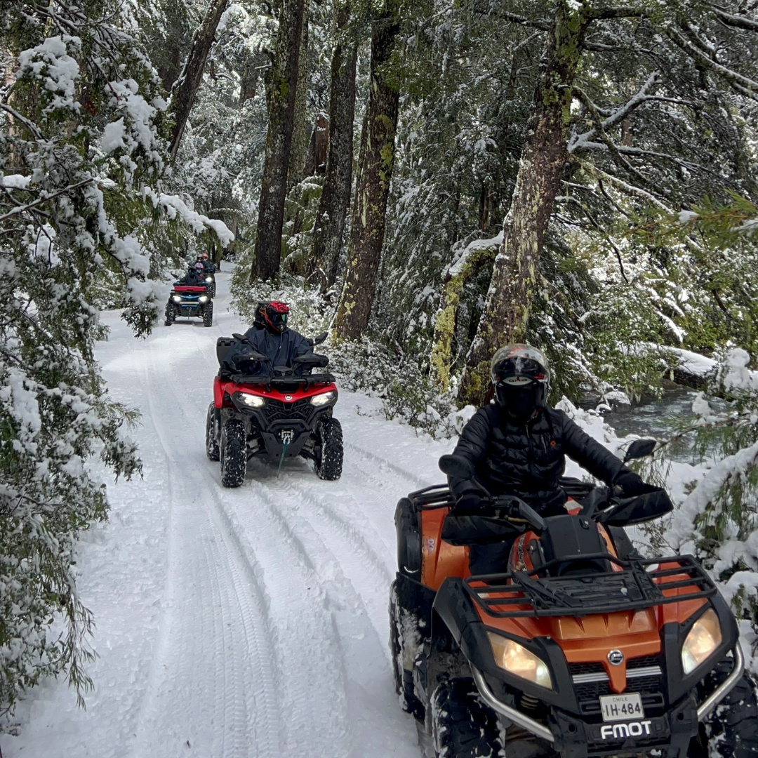 Grupo de personas recorriendo un sendero nevado en cuatrimotos 4x4 entre bosques de Coñaripe.